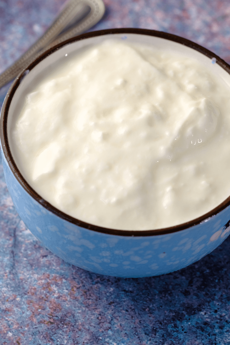 Oats in a wooden spoon next to a bowl of thick milk cream – gentle exfoliating winter scrub | skincaresolutions,in